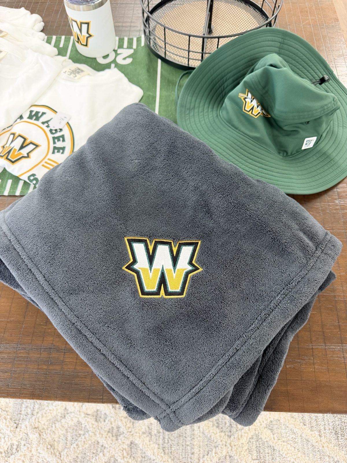 Grey fleece blanket with an embroidered W, beside a green bucket hat and a printed tee