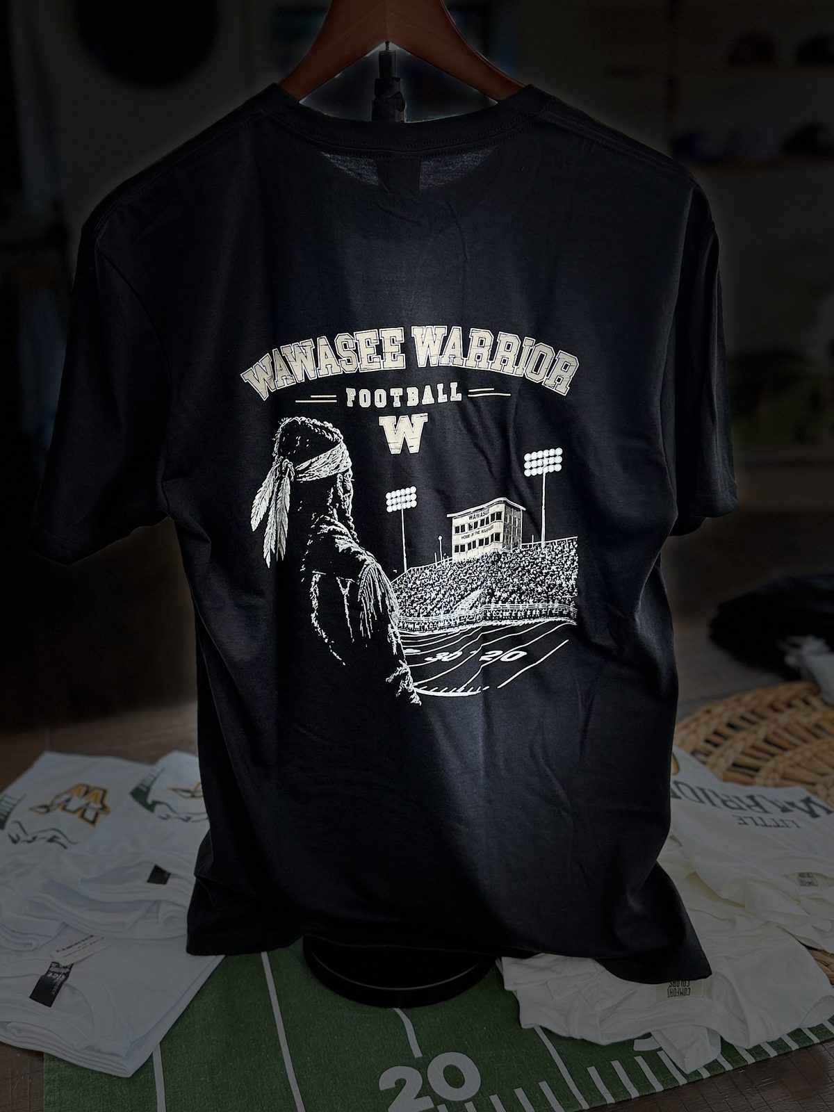 Black tee with a large cream full-back print of a warrior and the Wawasee football stadium