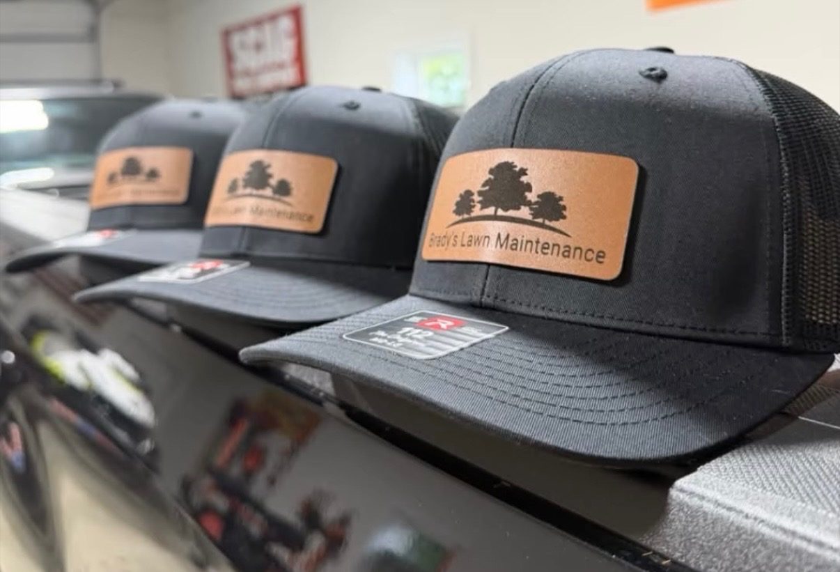 A row of black trucker caps with tan leather patches for Brady's Lawn Maintenance