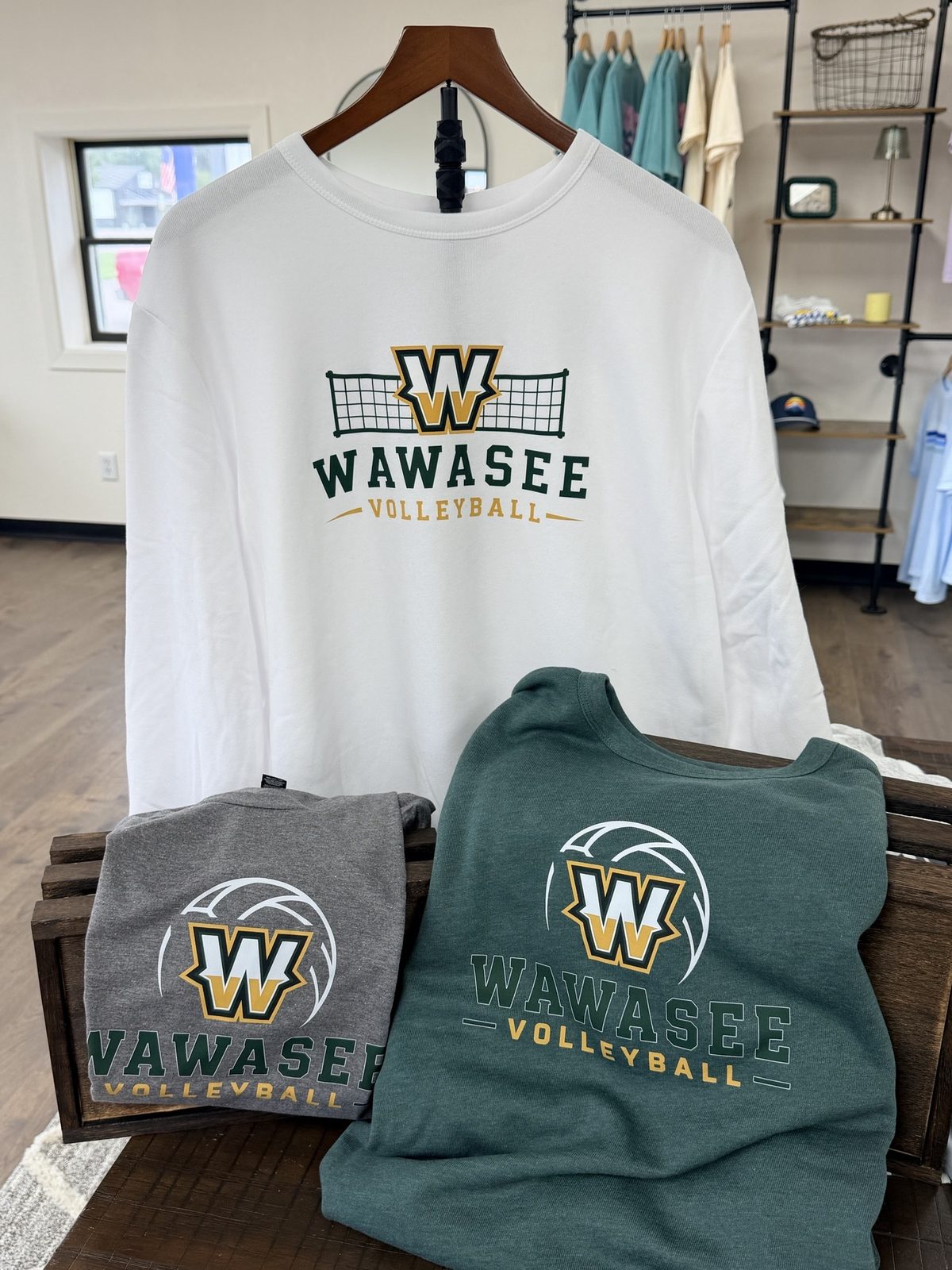 White, grey and green Wawasee Volleyball crewnecks and tees on display in the shop